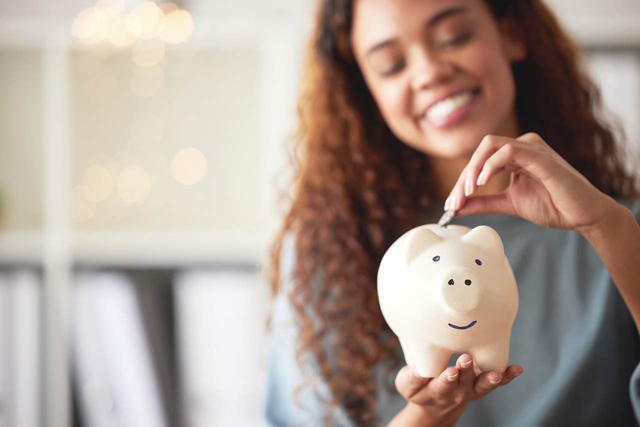 happy young mixed race woman holding a piggybank and depositing a coin as savings
