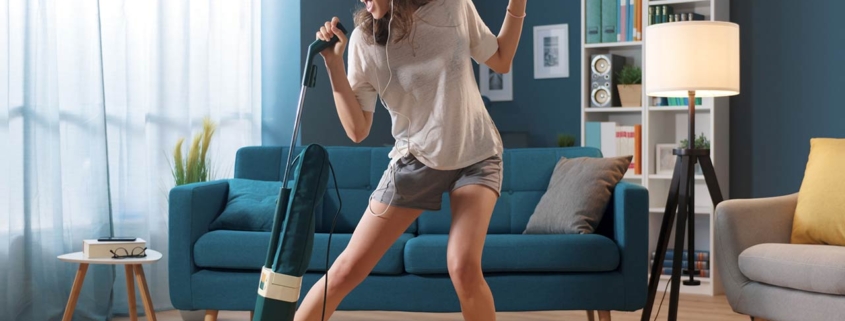 Cheerful woman cleaning up her home and singing, using the vacuum cleaner as a microphone