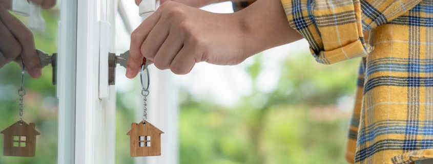 Man in a yellow plaid shirt using a key with house keychain to unlock a slider door