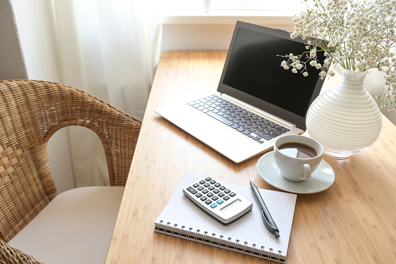 Home office desk with laptop computer, calculator, spiral book, coffee and a white flower bouquet, business accounting concept, copy space, selected focus